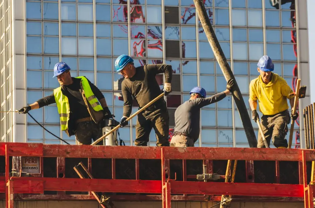 Four construction workers in hard hats and vests working on a skyscraper project.